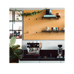 A countertop with espresso machine and a coffee mill. In the background is a pegboard shelf with knobs.