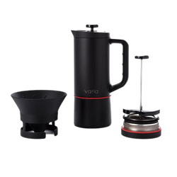 A black Varia coffee brewer with additional accessories including a paper filter, a brewing guide, and a user manual.